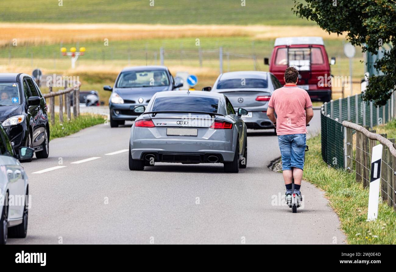 Ein Mann fährt mit seinem E-Trottinett auf einer dichtbefahrenenen Straße ausserorts im Zürcher Unterland. (Oberglatt, Schweiz, 01.07.2023) Stockfoto