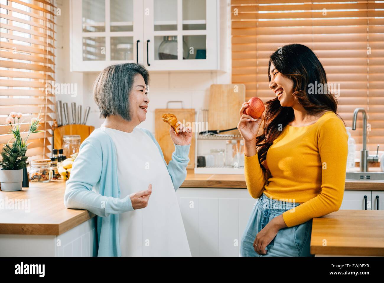 Eine ältere Mutter und ihre erwachsene Tochter, eine junge Frau in einer Schürze, verbinden sich mit Essen in der Küche Stockfoto