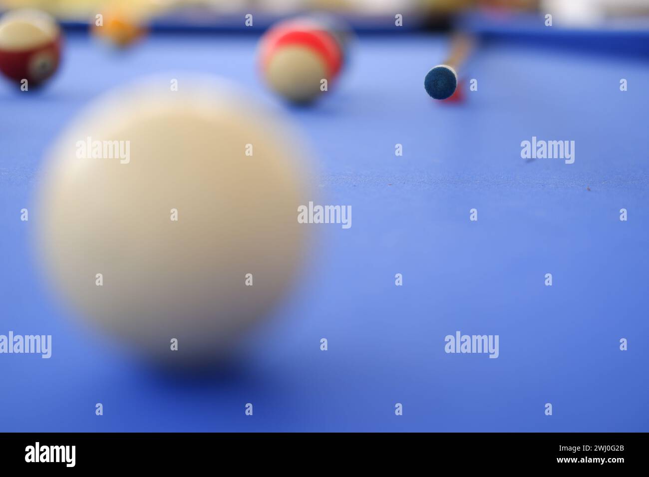 Billard-Kugeln und Billard-Queue sind an einem sonnigen Sommertag im Freien auf dem blauen Billard-Tisch. Queue auf dem Tisch, kurz vor dem Ball, Bokeh-Foto Stockfoto