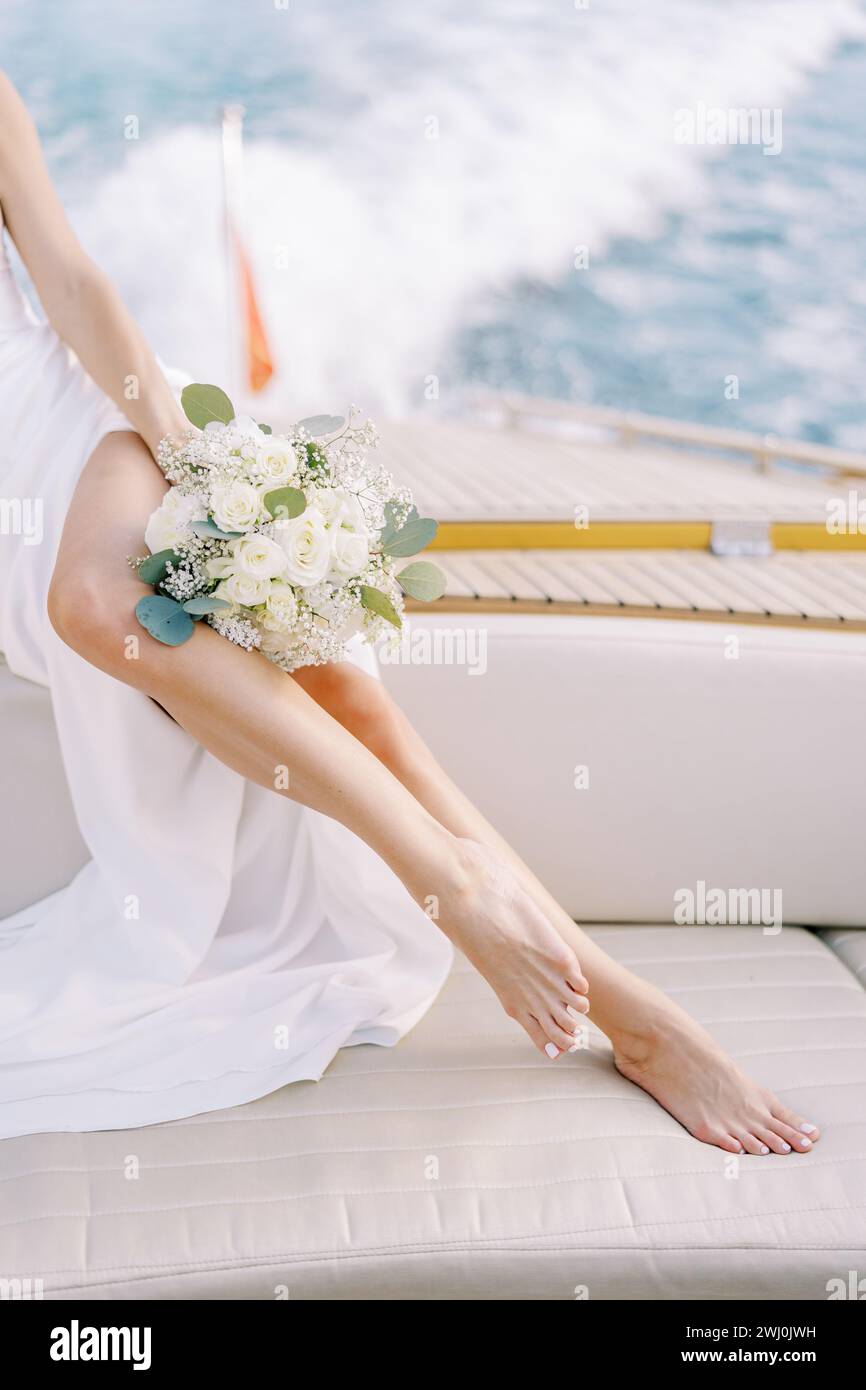 Braut mit einem Blumenstrauß sitzt an Bord einer Yacht, die auf dem Meer segelt. Abgeschnitten. Gesichtslos Stockfoto