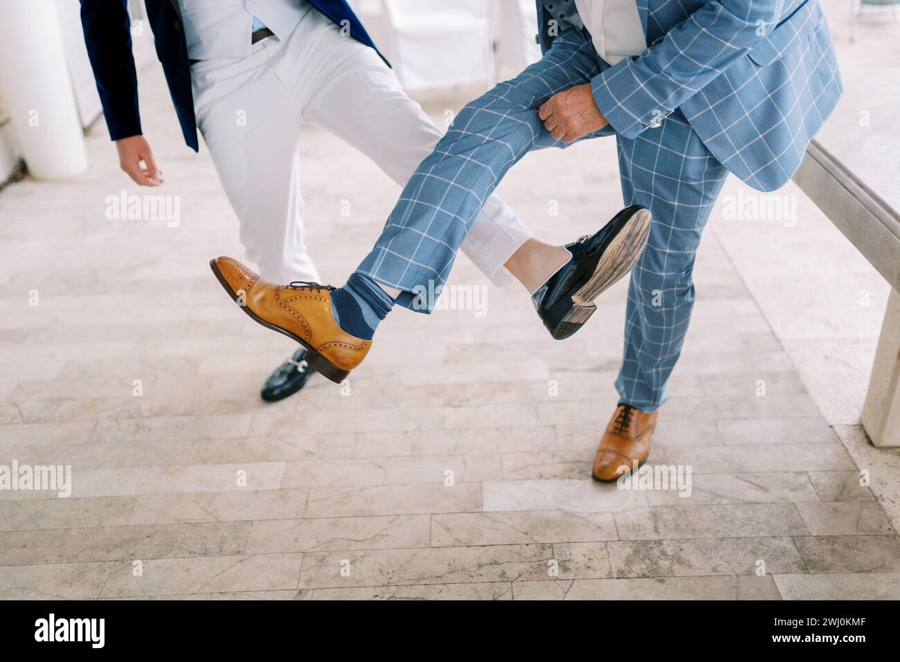 Bräutigam und bester Mann treten an, indem sie ihre Schuhe auf ihren ausgestreckten Beinen zeigen. Abgeschnitten. Gesichtslos Stockfoto