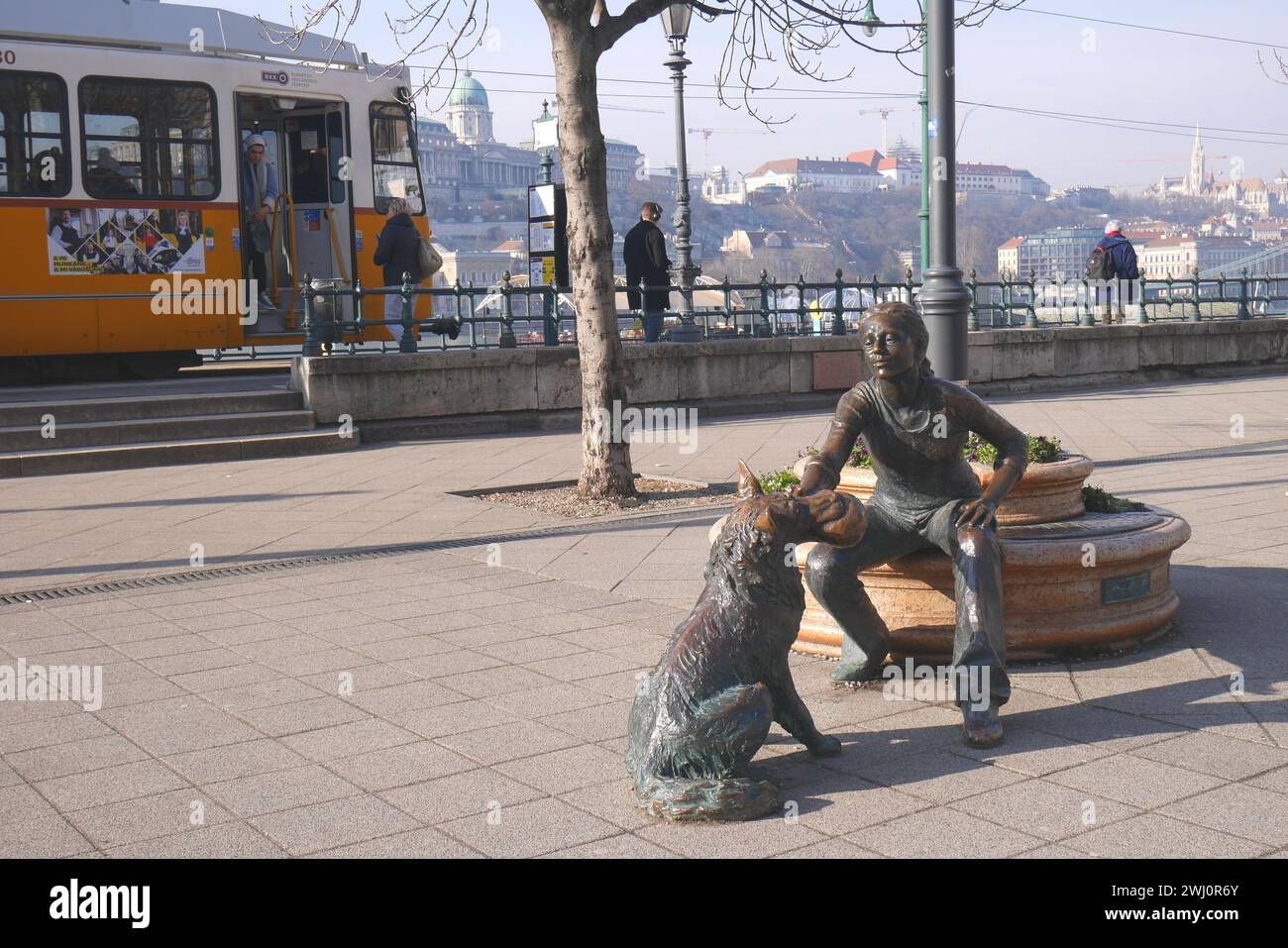 Bronzestatue eines Mädchens, das mit einem Hund spielt, mit einer Straßenbahn dahinter, von Raffay Dávid, Donaudamm, Pest, Budapest, Ungarn Stockfoto