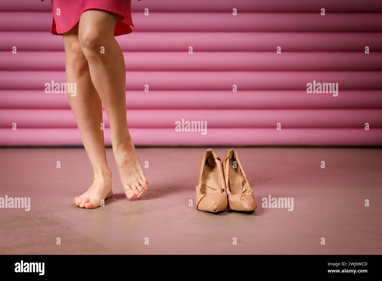 Weibliche Beine ziehen hohe Schuhe an, die in rustikalem beigefarbenem Bastelpapier auf rosa Hintergrund gewickelt sind. Black Friday-Konzept Stockfoto