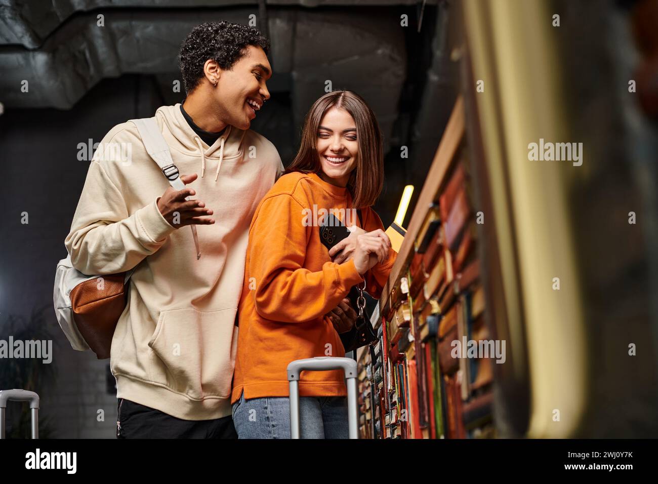 Glücklicher schwarzer Mann, der mit einer fröhlichen Frau spricht, die am Rezeptionsschalter im Hostel eine Kreditkarte hält Stockfoto