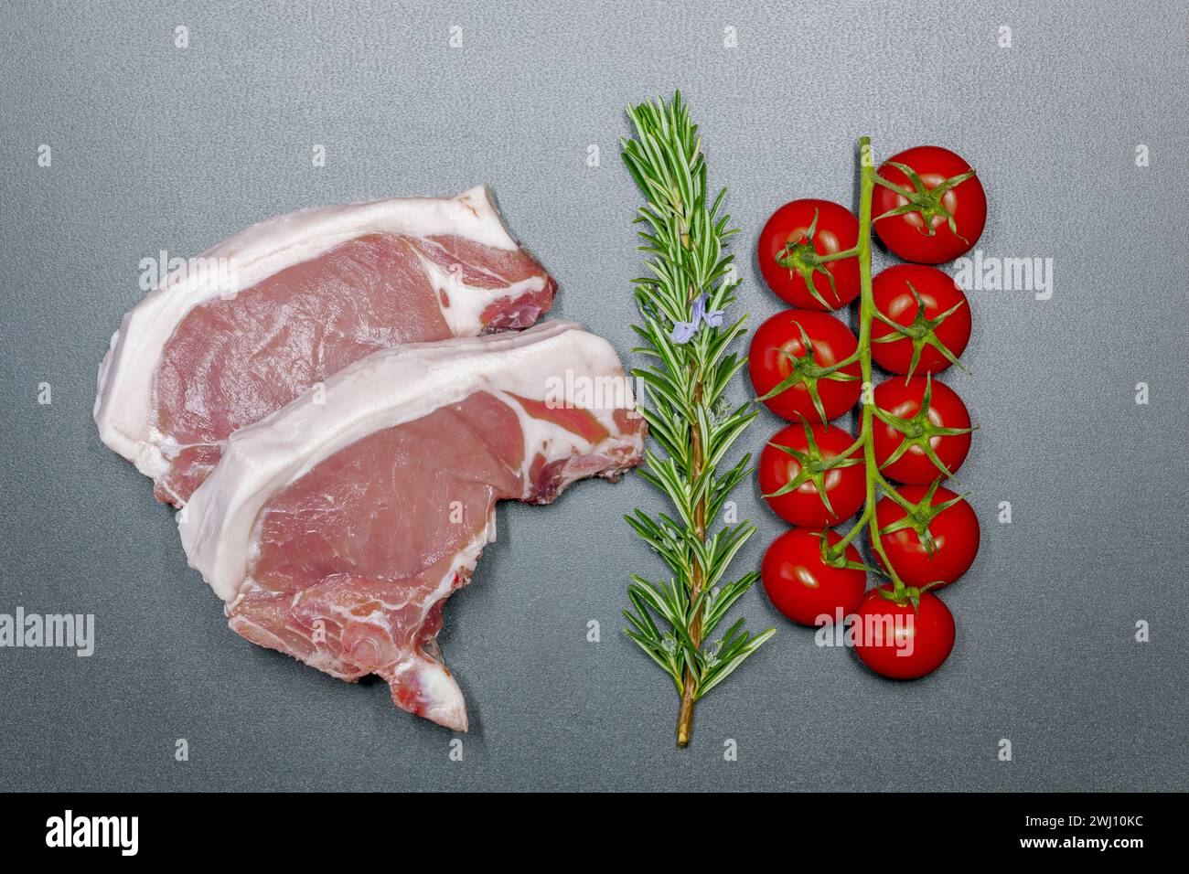 Geschnittenes rohes Schweinefleisch auf schwarzem Hintergrund. Frische Schweinekoteletts mit Rosmarin und Cocktail Stockfoto