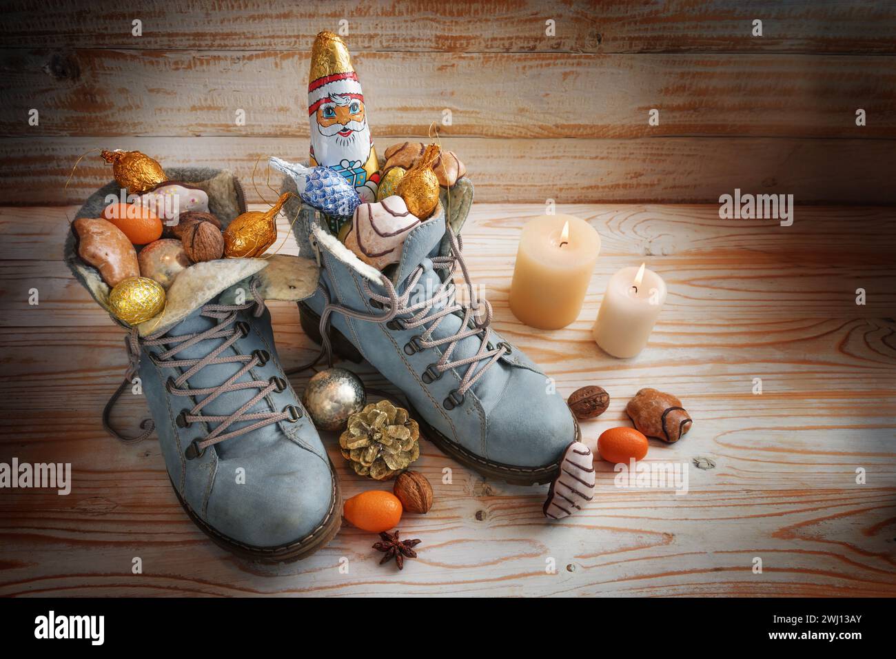 Stiefel gefüllt mit Süßigkeiten, Schokolade Santa und Weihnachtsdekoration auf hölzernem Hintergrund mit Kerzen, Tradition auf deutscher Niko Stockfoto
