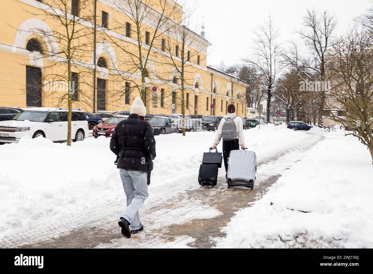 RIGA, LETTLAND. März 2023. Touristen mit Gepäck spazieren auf schneebedecktem Gehweg. Stockfoto