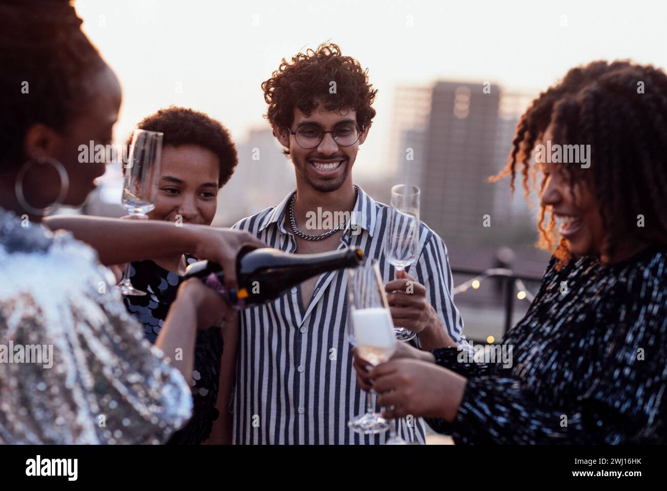 Dunkelhäutiges Mädchen gießt Champagner in Gläser ihrer multinationalen Freunde Stockfoto