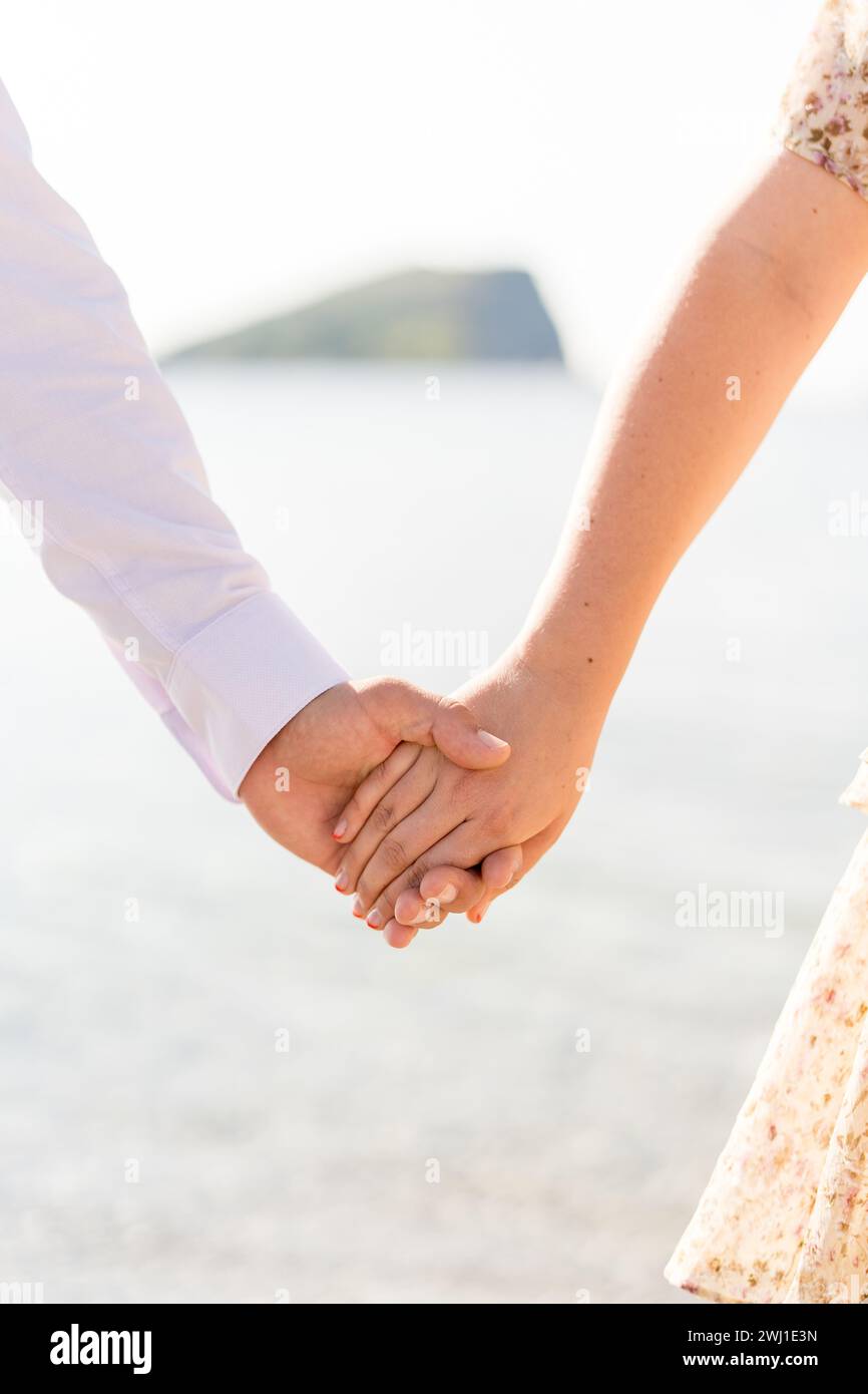 Der Mann hält die Hand der Frau, während er am Meer steht. Abgeschnitten. Gesichtslos Stockfoto