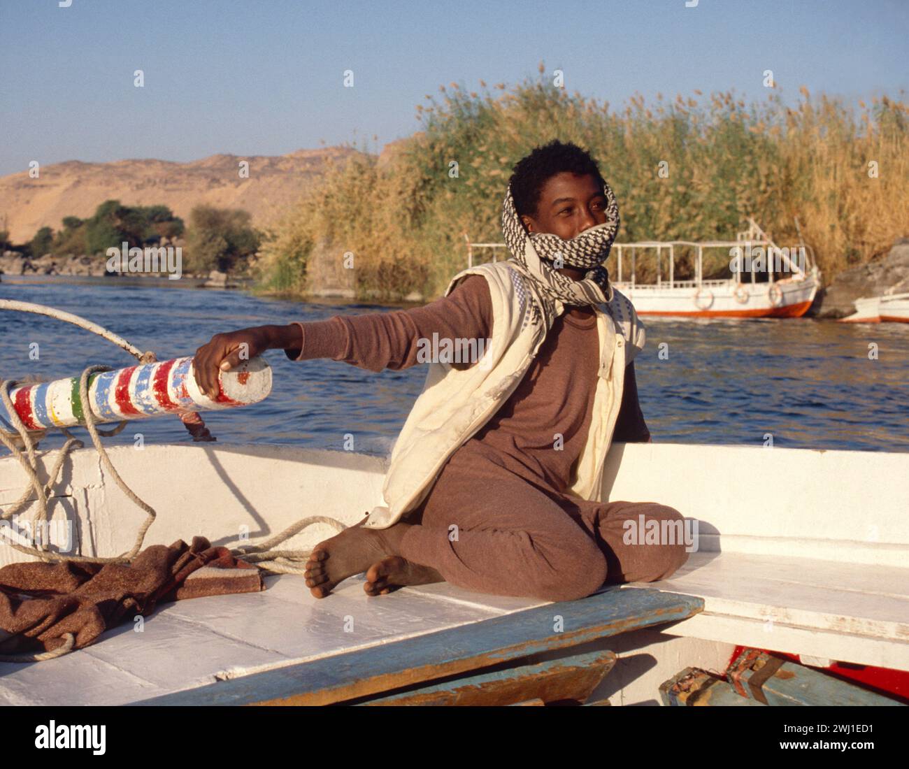 Ägypten. Assuan. Nubischer Junge auf dem Tiller des Felucca Segelbootes auf dem Nil. Stockfoto