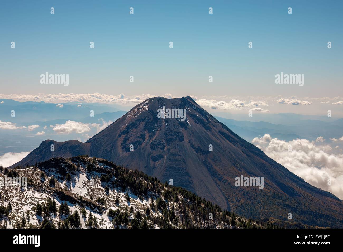 Schneebedeckte Berge überragen über einer Decke aus schneebedeckten Wolken mit einer entfernten Mittelgebirgskette Stockfoto