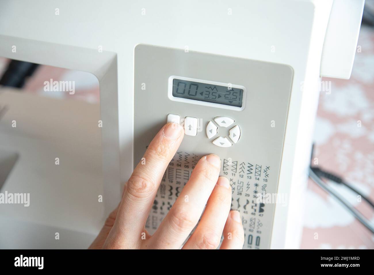 Detail einer Hand, die die Taste drückt, um einen Stich für maschinelles Nähen auszuwählen. Tabelle der Nähoptionen für die Elektromaschine. Stockfoto