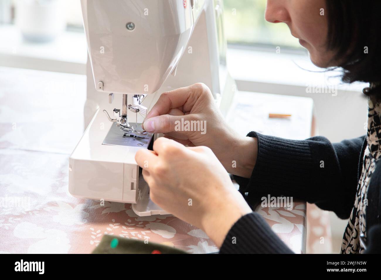 Die Hand der Frau vor der Nähmaschine, um die Nadel zu fädeln und dann zu nähen. Präzision und winzige Details. Stockfoto