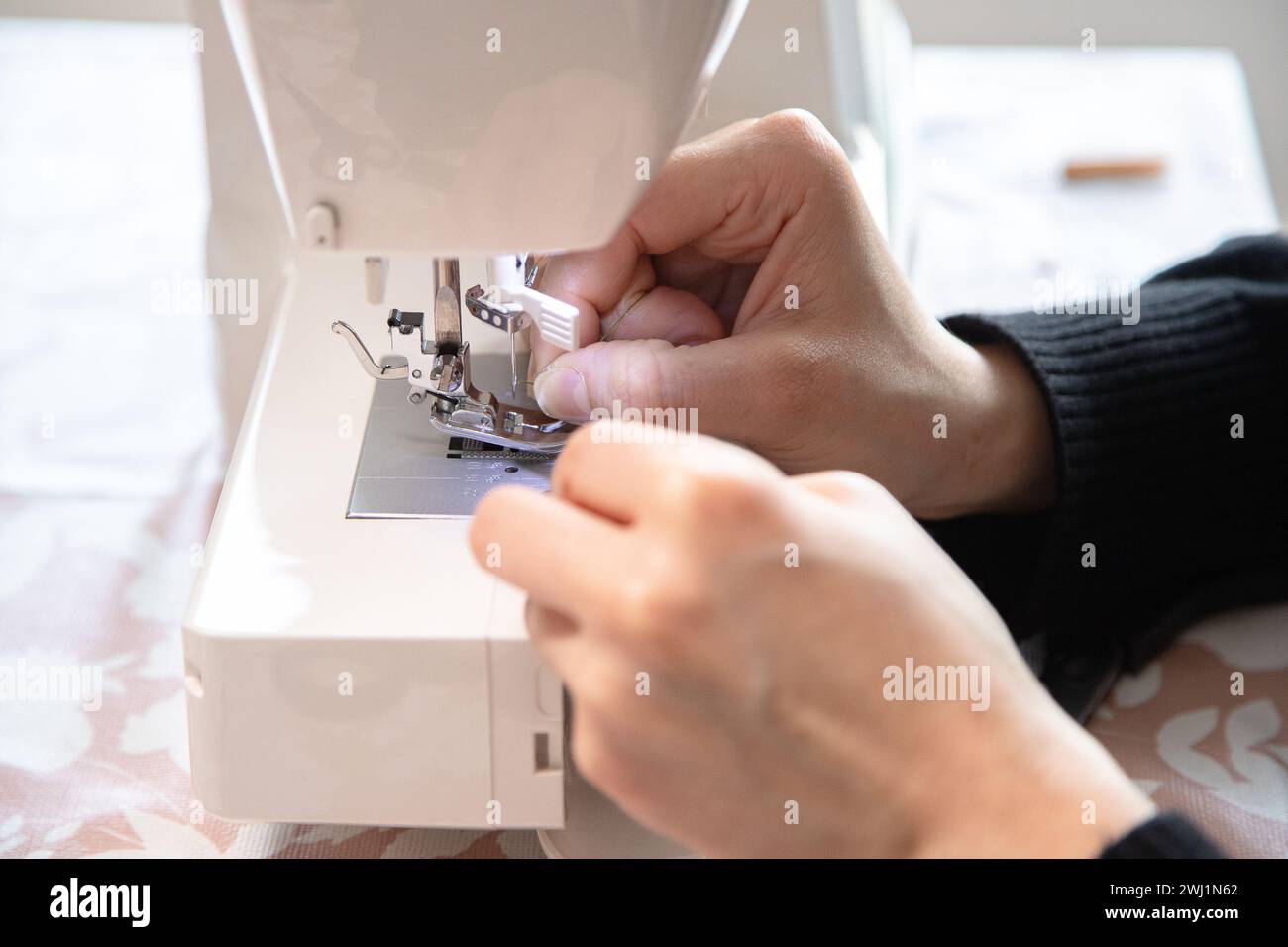 Die Hand der Frau vor der Nähmaschine, um die Nadel zu fädeln und dann zu nähen. Präzision und winzige Details. Stockfoto