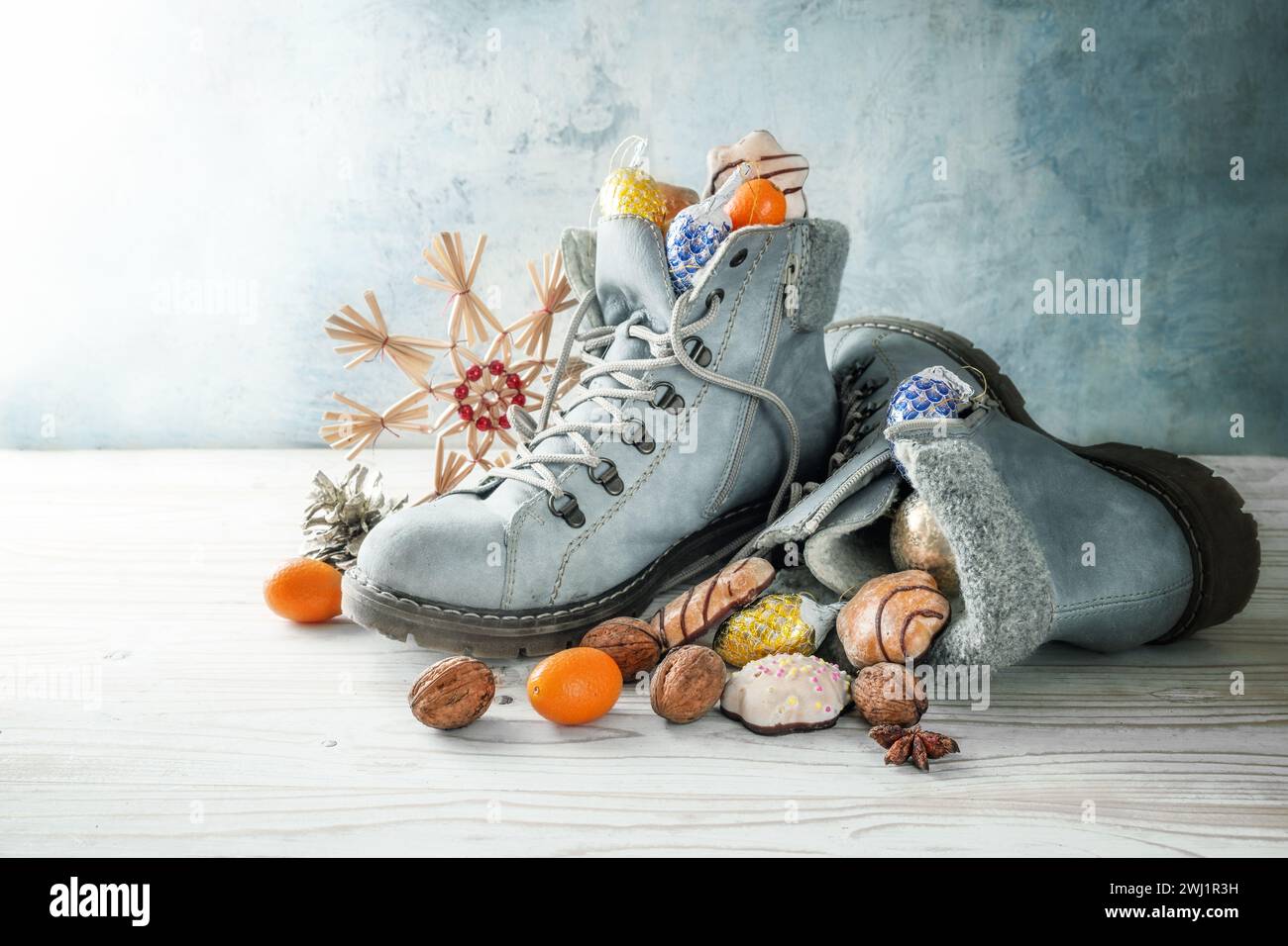 Nikolaus Tag oder in Deutschland Nikolaus Tag im Dezember, Winterstiefel gefüllt mit Leckereien und Weihnachtsdekoration gegen eine kalte blu Stockfoto
