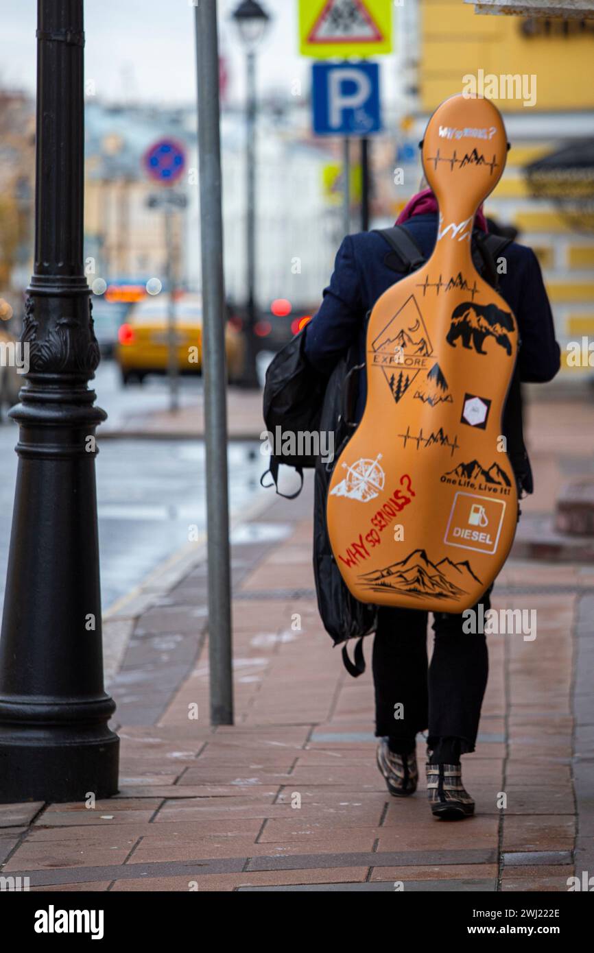Ein Musiker, der mit einem Cello-Etui mit Inschriften und Bildern herumläuft, unter ihnen ist „Warum so ernst?“ Stockfoto