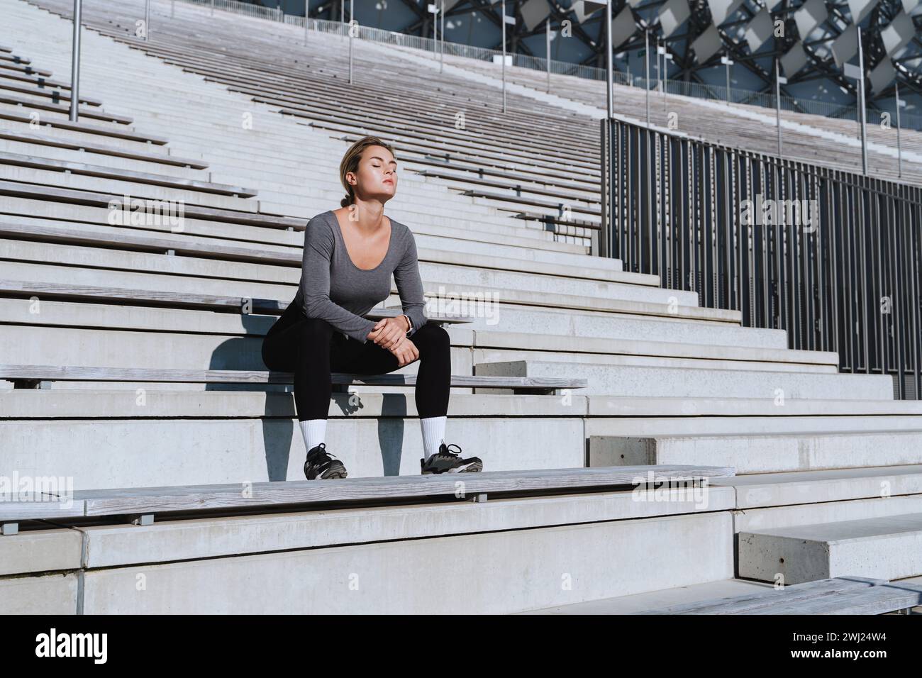 Sportlerin in weiblicher Sportbekleidung, die auf der Bank von Tribünen im Freiluftstadion sitzt Stockfoto