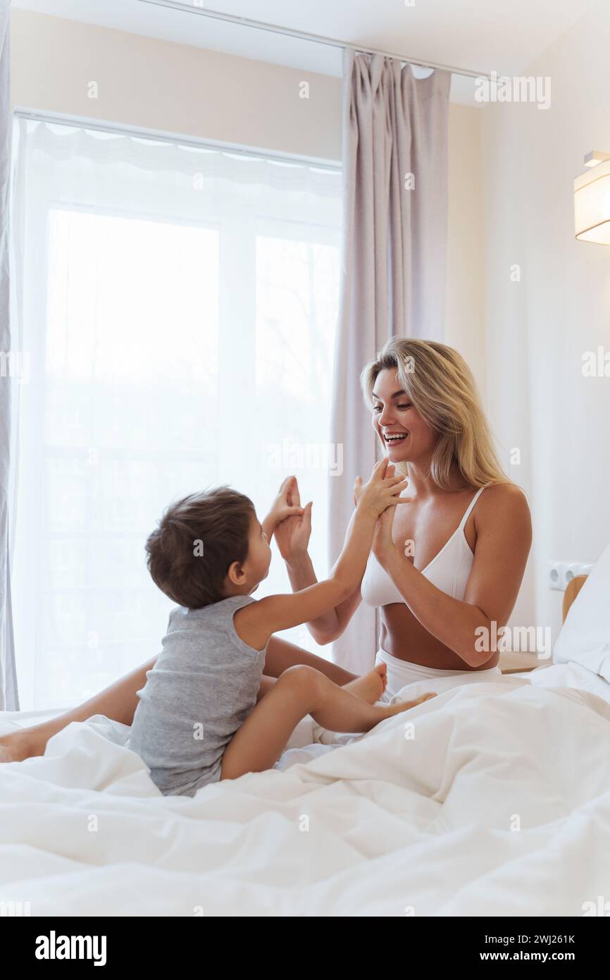 Die glückliche Mutter und ihr kleiner Sohn spielen fröhlich und schaffen wertvolle Erinnerungen, während sie sich im Komfort ihres Bettes verbinden Stockfoto