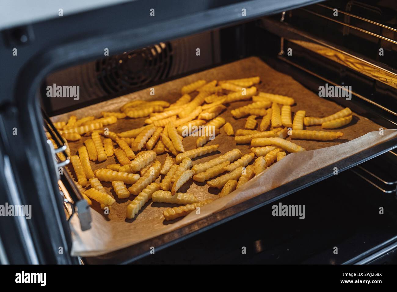 Knusprige Pommes Frites verteilen sich auf einem mit Backpapier ausgelegten Backblech Stockfoto