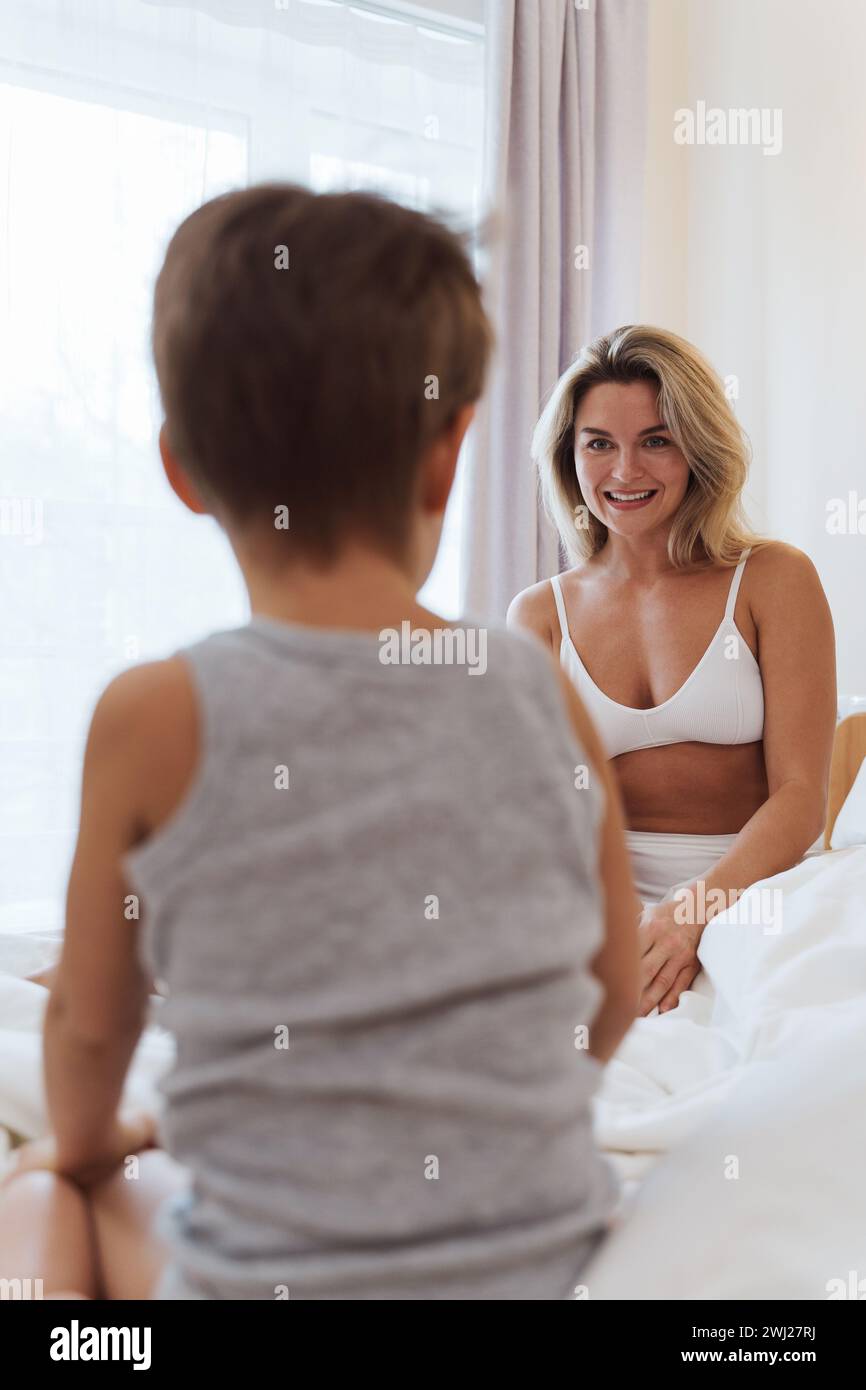 Die glückliche Mutter und ihr kleiner Sohn spielen fröhlich und schaffen wertvolle Erinnerungen, während sie sich im Komfort ihres Bettes verbinden Stockfoto