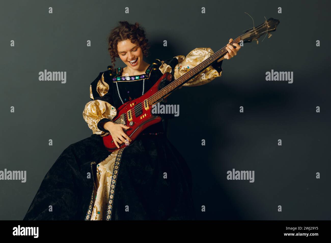 Porträt einer jungen erwachsenen Frau, die Musik auf elektrischer Gitarre spielt und in einem mittelalterlichen Kleid gekleidet ist. Stockfoto