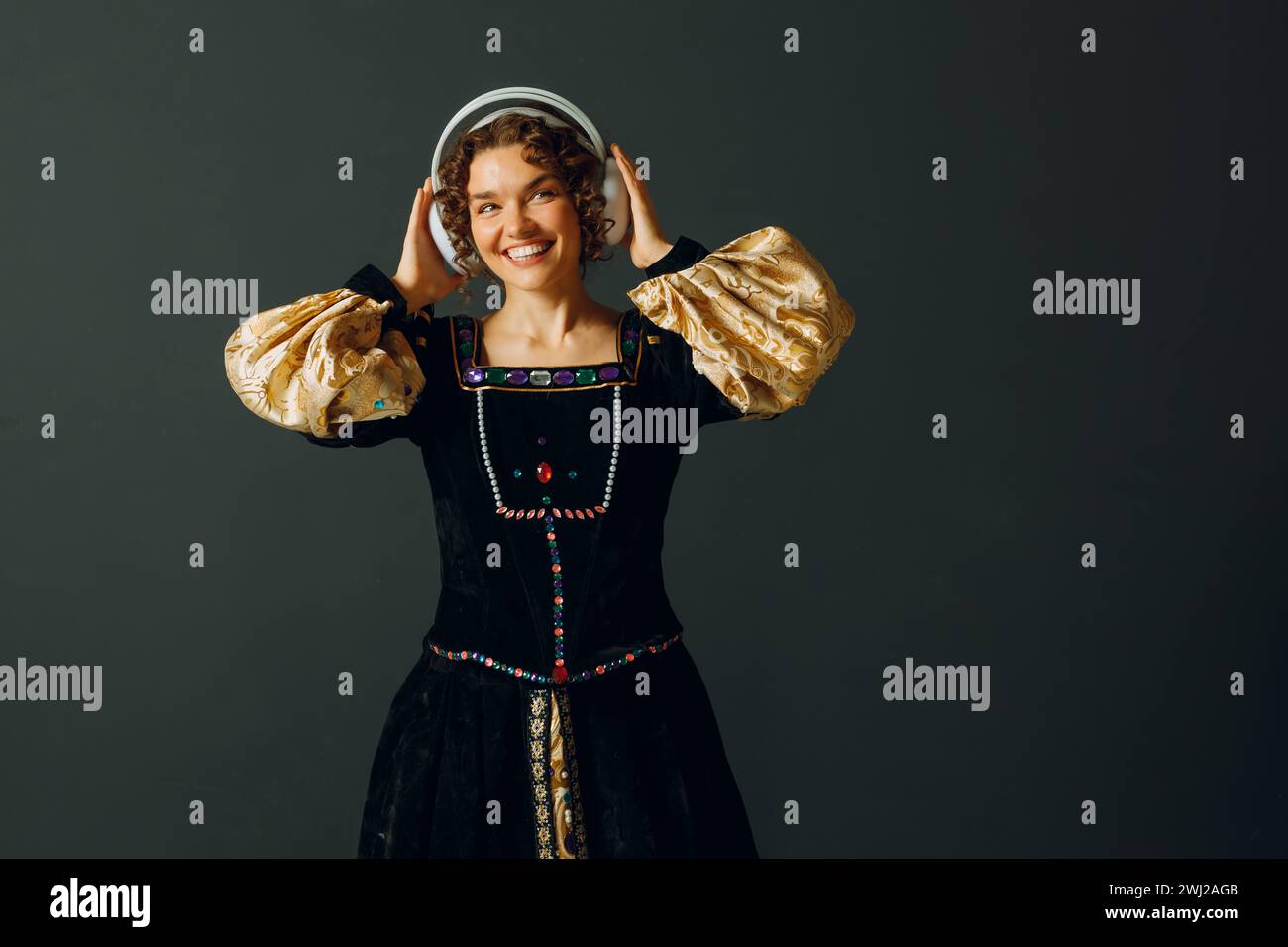 Porträt einer jungen Renaissance-Frau mit Kopfhörern und berührendem Kopf, in einem mittelalterlichen Kleid gekleidet, hört Musik. Stockfoto