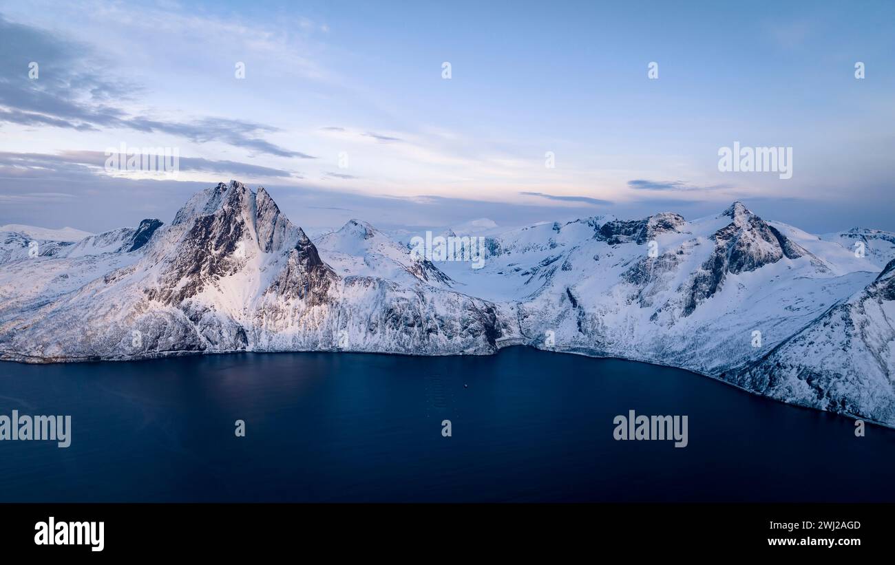 Drohnenaufnahme von schneebedeckten Bergen vor dem Meer gegen den Himmel in der Abenddämmerung Stockfoto