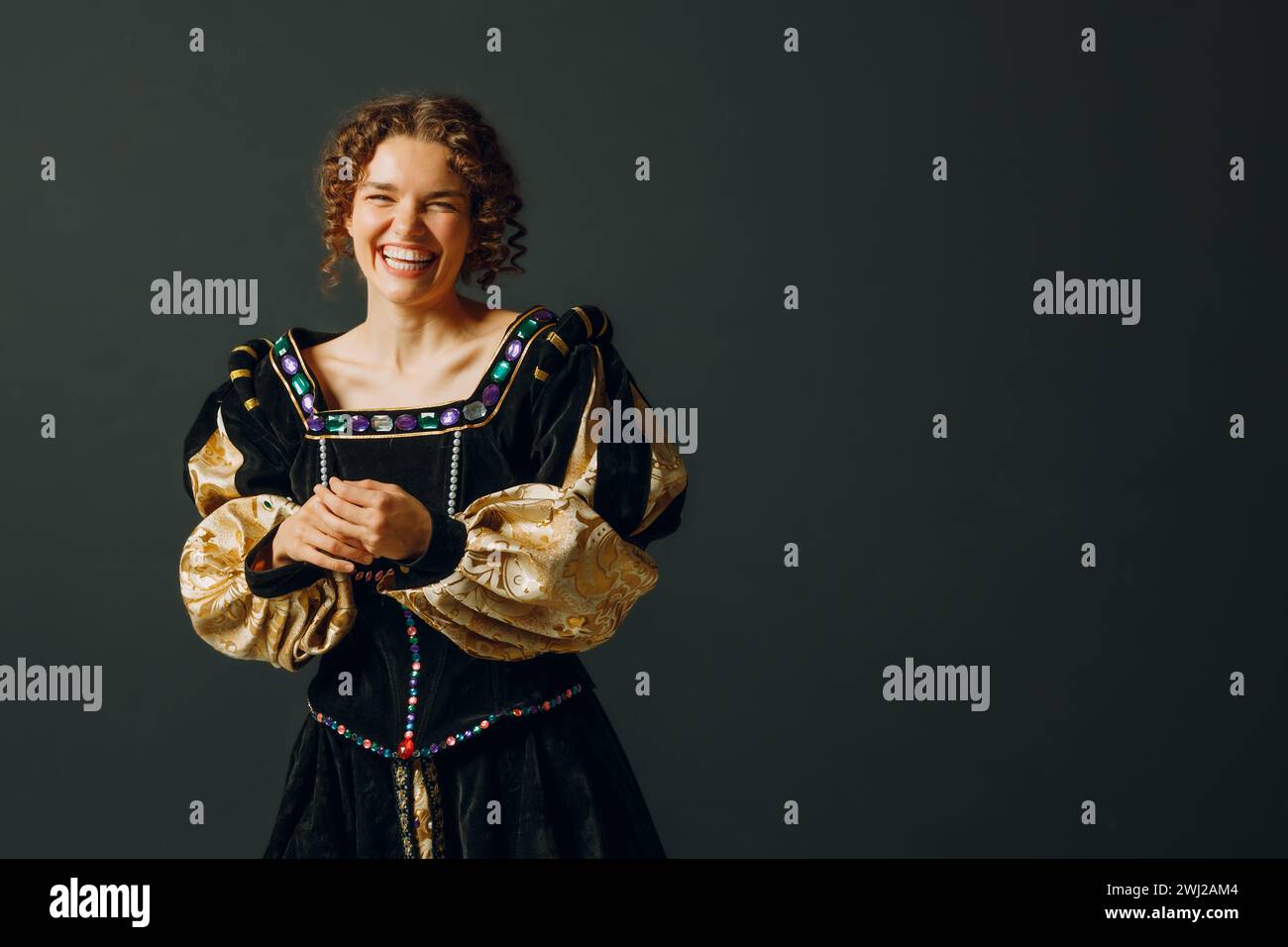 Porträt einer jungen lachenden Frau in einem mittelalterlichen Kleid auf dunklem Hintergrund. Stockfoto