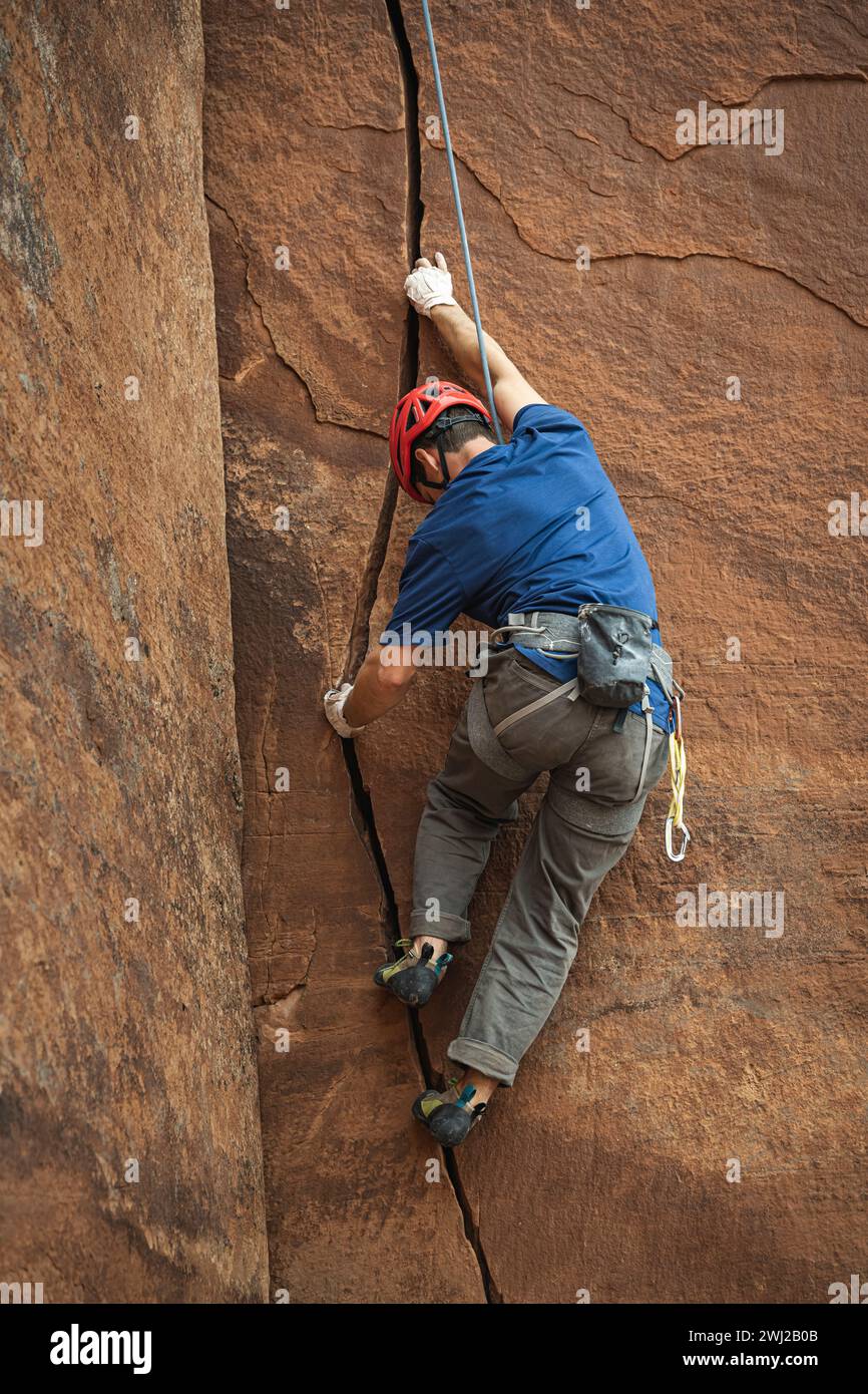 Entschlossener männlicher Bergsteiger, der felsige Klippen in der Wüste klettert Stockfoto