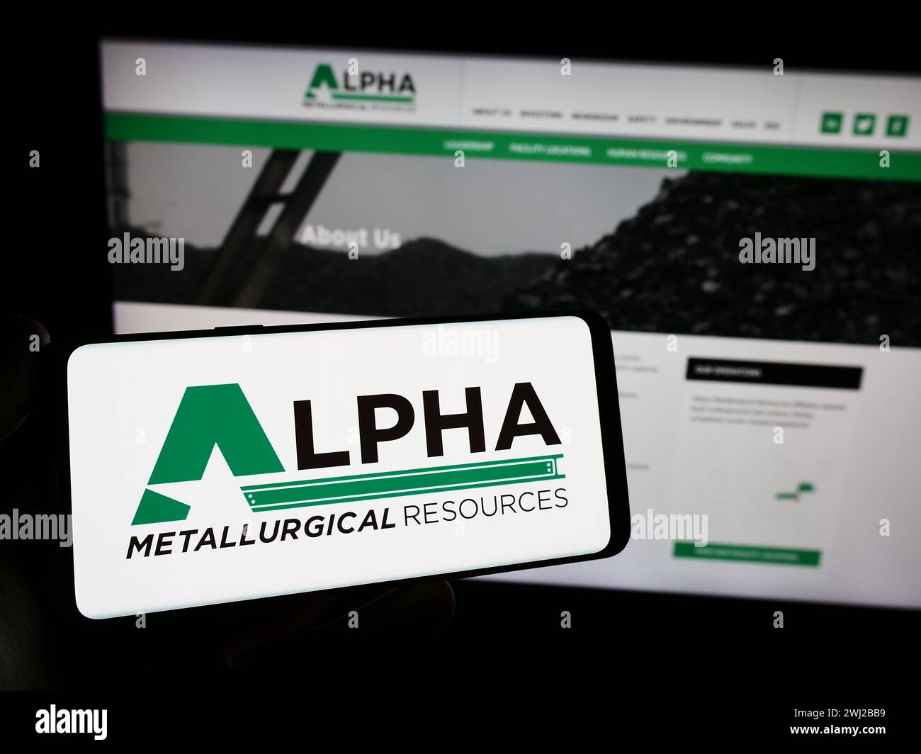 Person mit Smartphone und Logo des US-Bergbauunternehmens Alpha Metallurgical Resources Inc. Vor der Website. Schwerpunkt auf dem Display des Telefons. Stockfoto