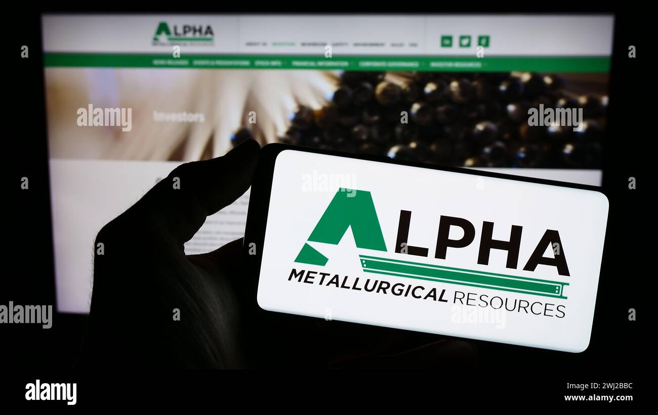 Person, die ein Mobiltelefon mit dem Logo des amerikanischen Bergbauunternehmens Alpha Metallurgical Resources Inc. Vor der Webseite hält. Schwerpunkt auf dem Display des Telefons. Stockfoto