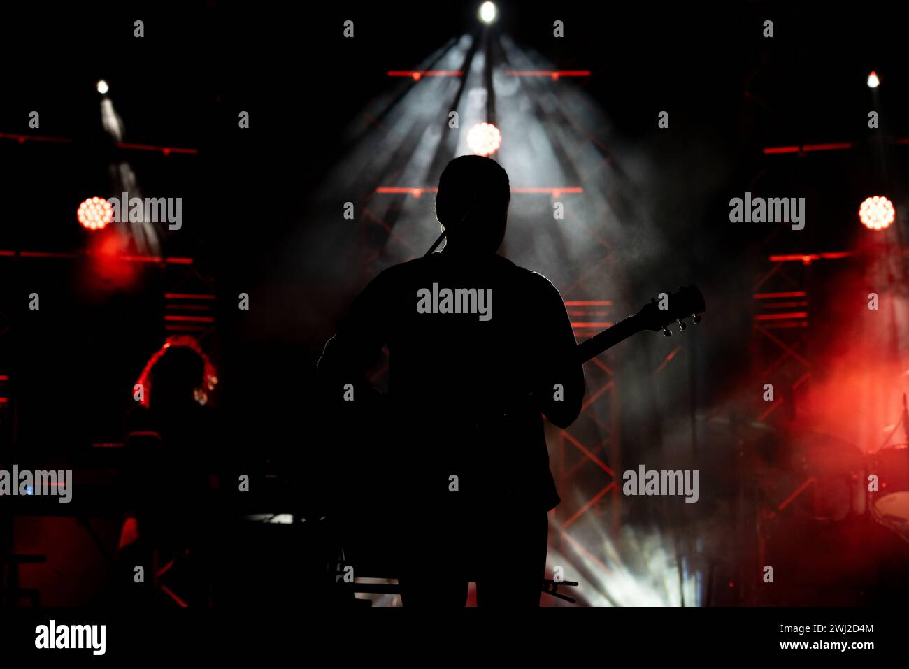 Musiker, der Gitarre spielt, spielt auf der Bühne unter Scheinwerferlicht. Silhouette eines Musikkünstlers und einer Band Stockfoto