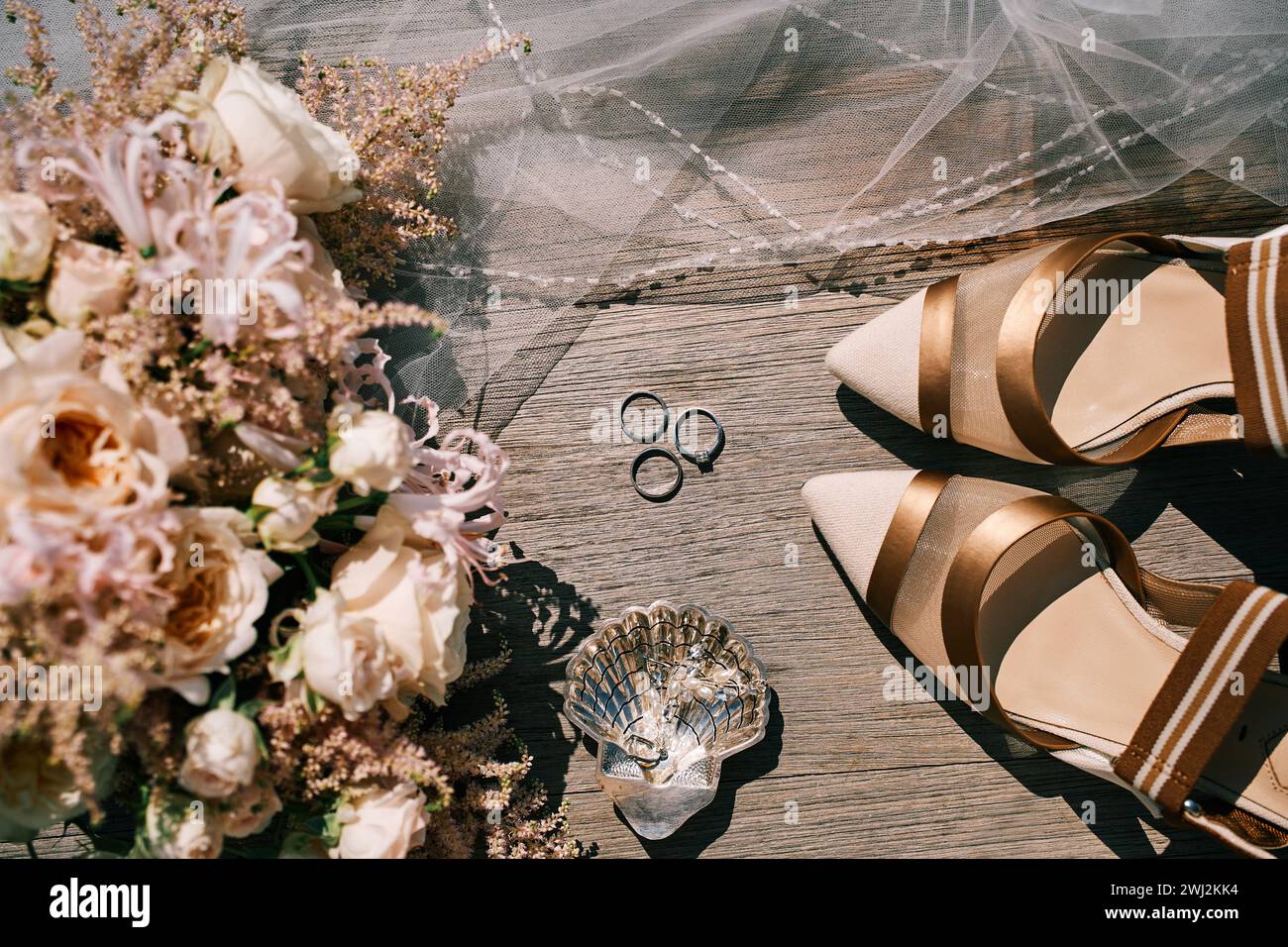 Hochzeitsringe, Brautschuhe und ein Blumenstrauß liegen auf einem Holztisch. Draufsicht Stockfoto