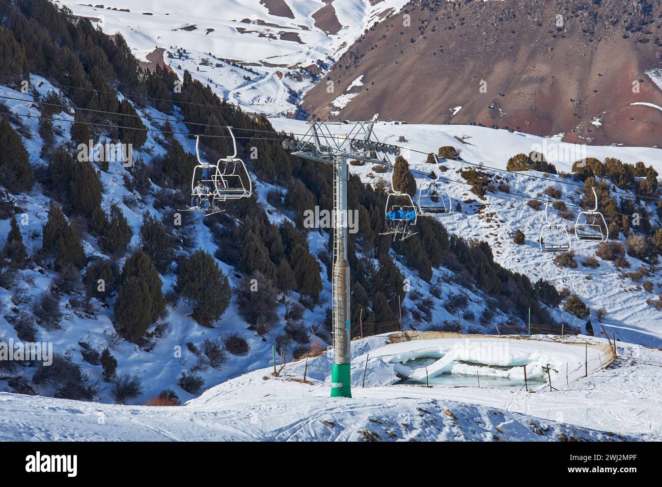 Skifahrer und Snowboarder fahren mit einem Skilift hinauf, der zum Gipfel der Berghänge führt. Seilbahnstange, Bau. Winterurlaub Aktivität, Lifestyle. Stockfoto