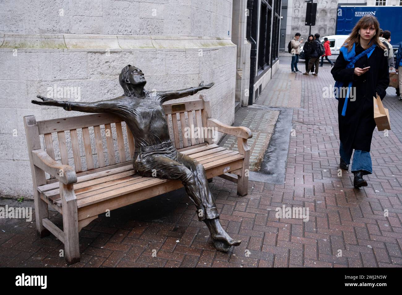 Skulptur des Beatles-Sängers John Lennon mit breiten Armen auf einer Bank in der Carnaby Street in einem Werk Imagine von Lawrence Holofcener am 9. Februar 2024 in London. Stockfoto