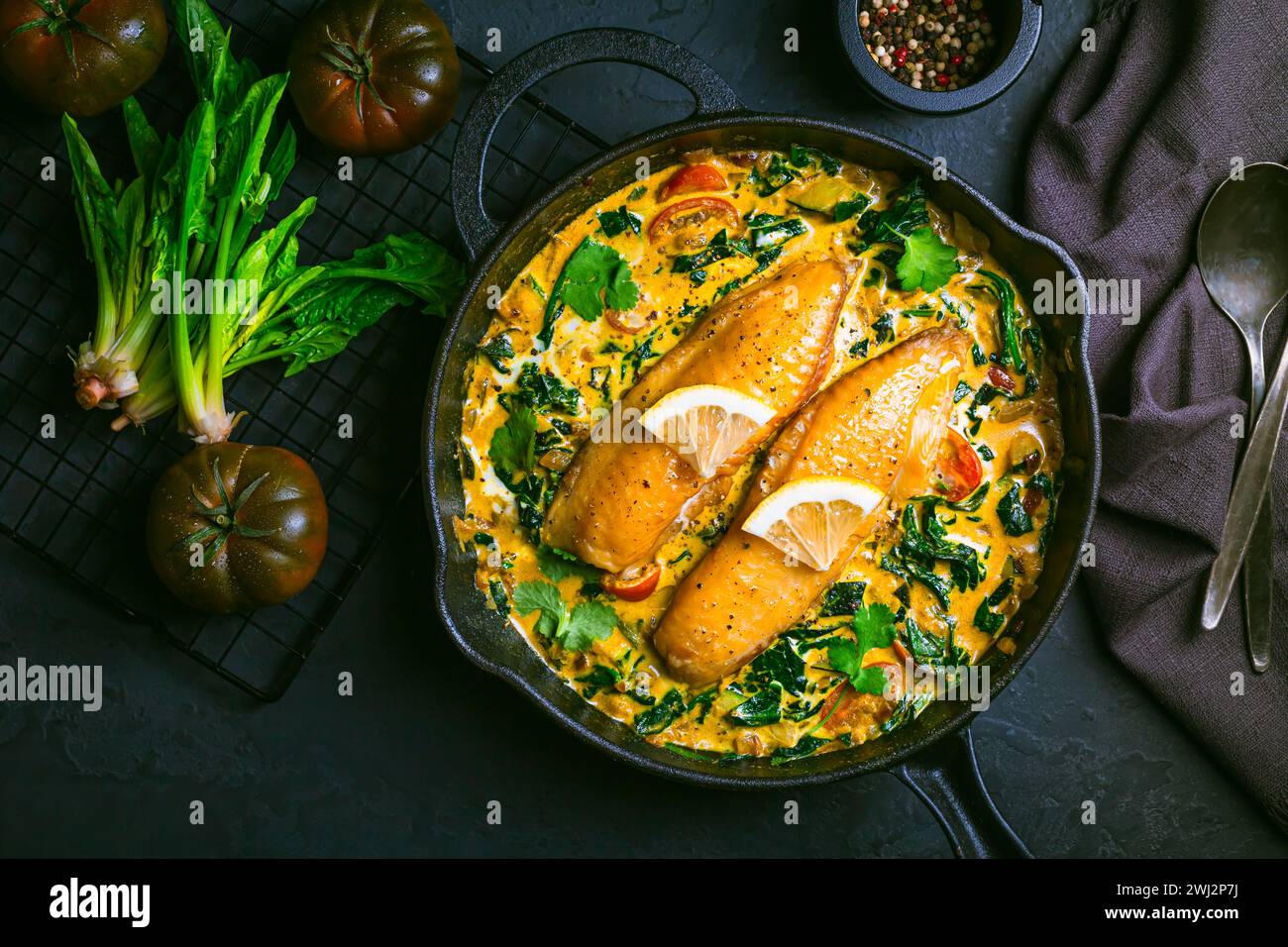 Rotes Curry mit Spinat, Kokosmilch und gebackenem Fisch in einer Pfanne Stockfoto