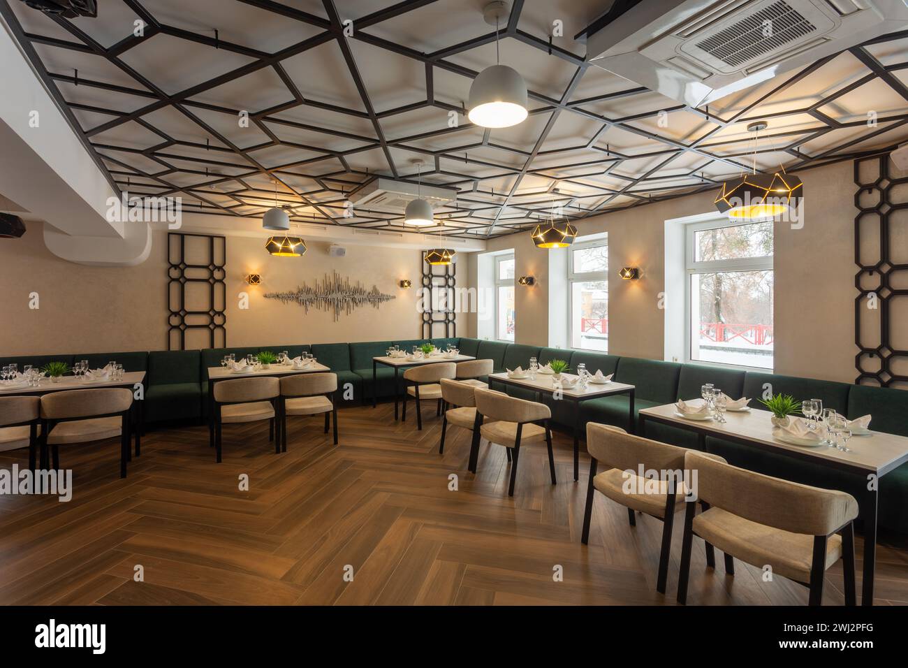 Modernes Interieur eines städtischen Restaurants oder Cafés mit Restaurants. Sanfte grüne Sofas und beige Stühle an Tischen, serviert mit Gläsern, Tellern und Servietten Stockfoto