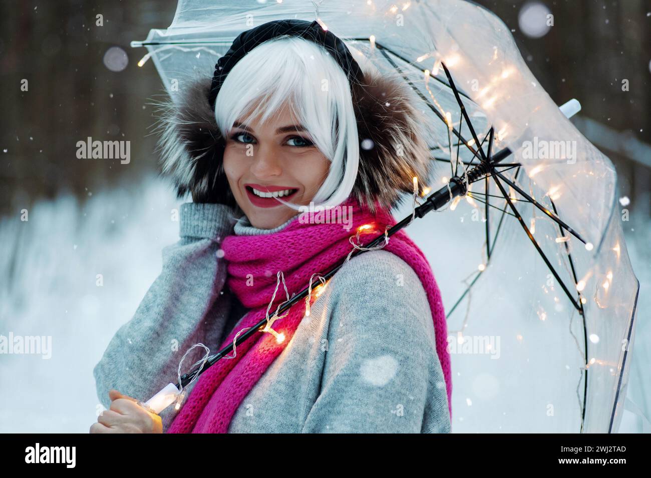 Frau, hält einen transparenten Regenschirm, eingebettet in funkelnde Lichter, die eine magische Winteratmosphäre schaffen Stockfoto