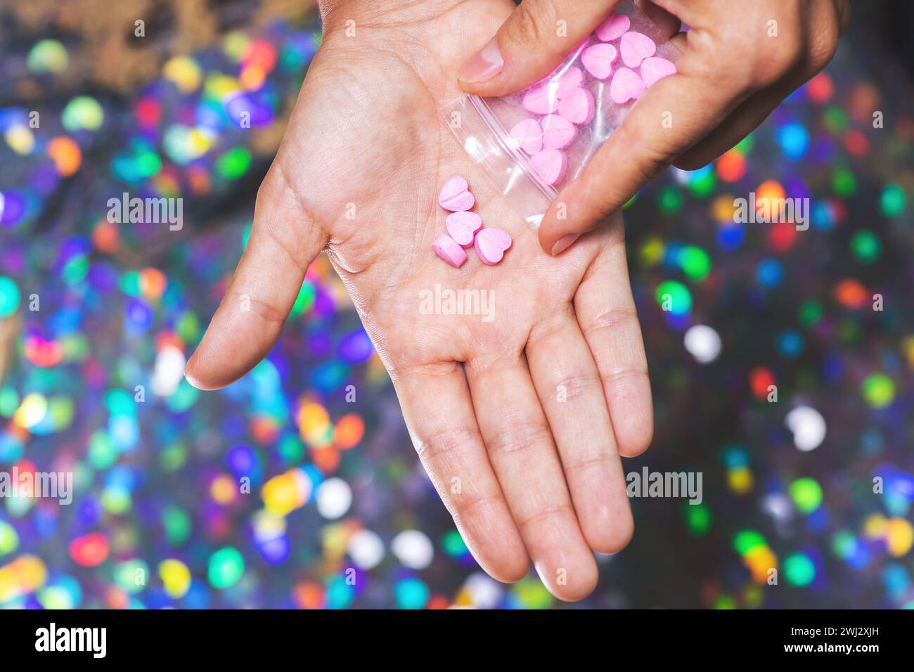 Mann, der herzförmige Pillen aus dem Reißverschlussbeutel auf die Handfläche gießt. Stockfoto