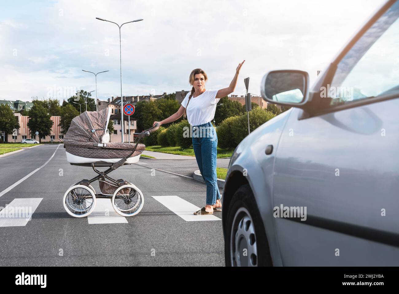 Eine empörte Mutter mit dem Kinderwagen, der mit einem Autofahrer auf dem Straßenübergang in Konflikt steht Stockfoto