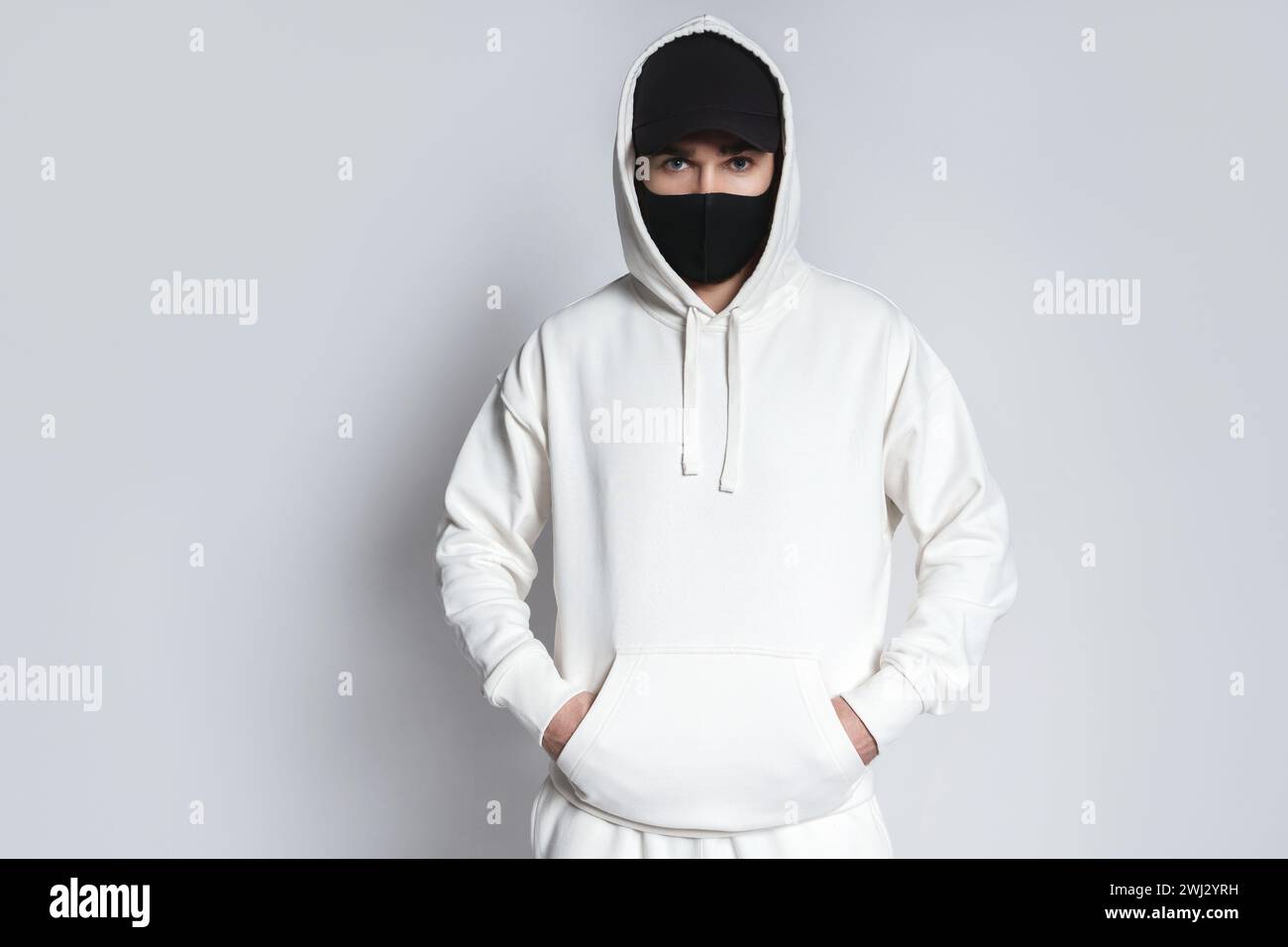 Mann mit weißem Hoodie, schwarzer Baseballmütze und Stoffmaske Stockfoto