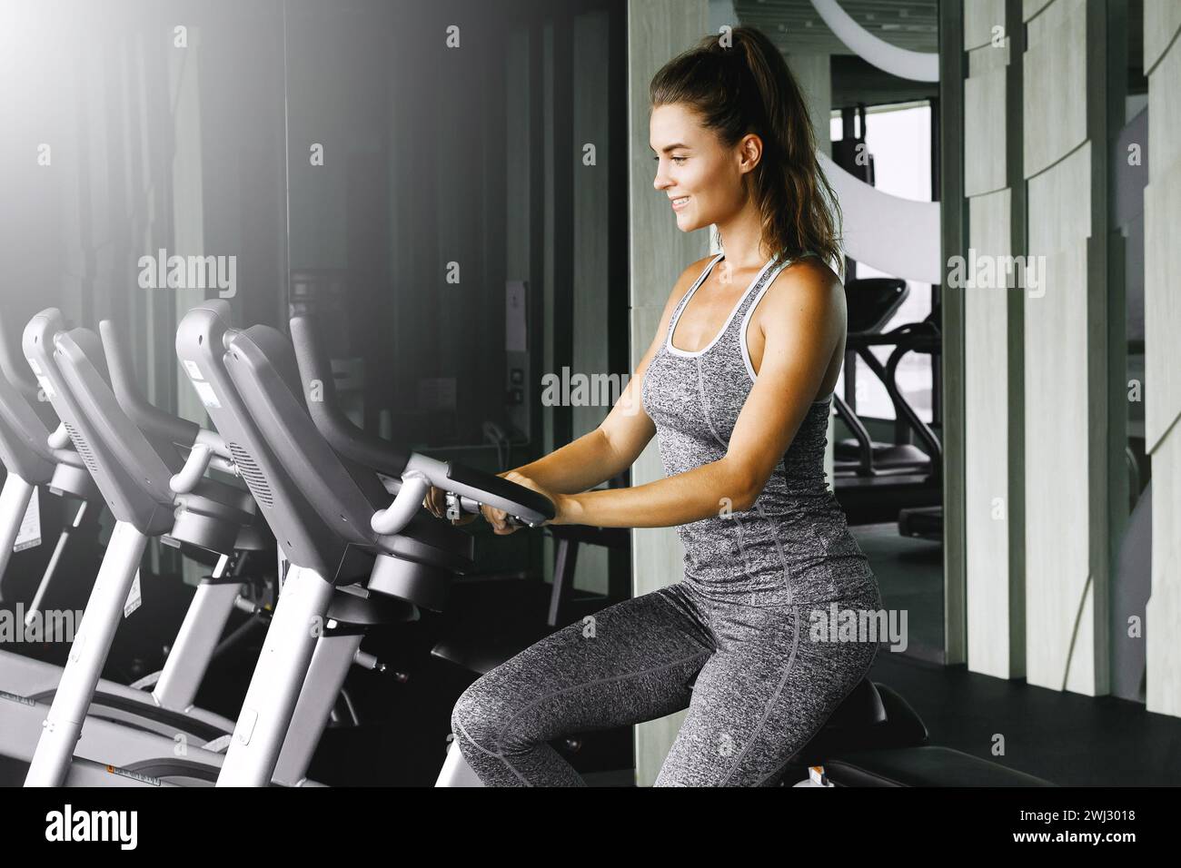 Fröhliche Frau radelt während ihres Cardio-Workouts im Fitnessstudio auf dem Heimtrainer Stockfoto