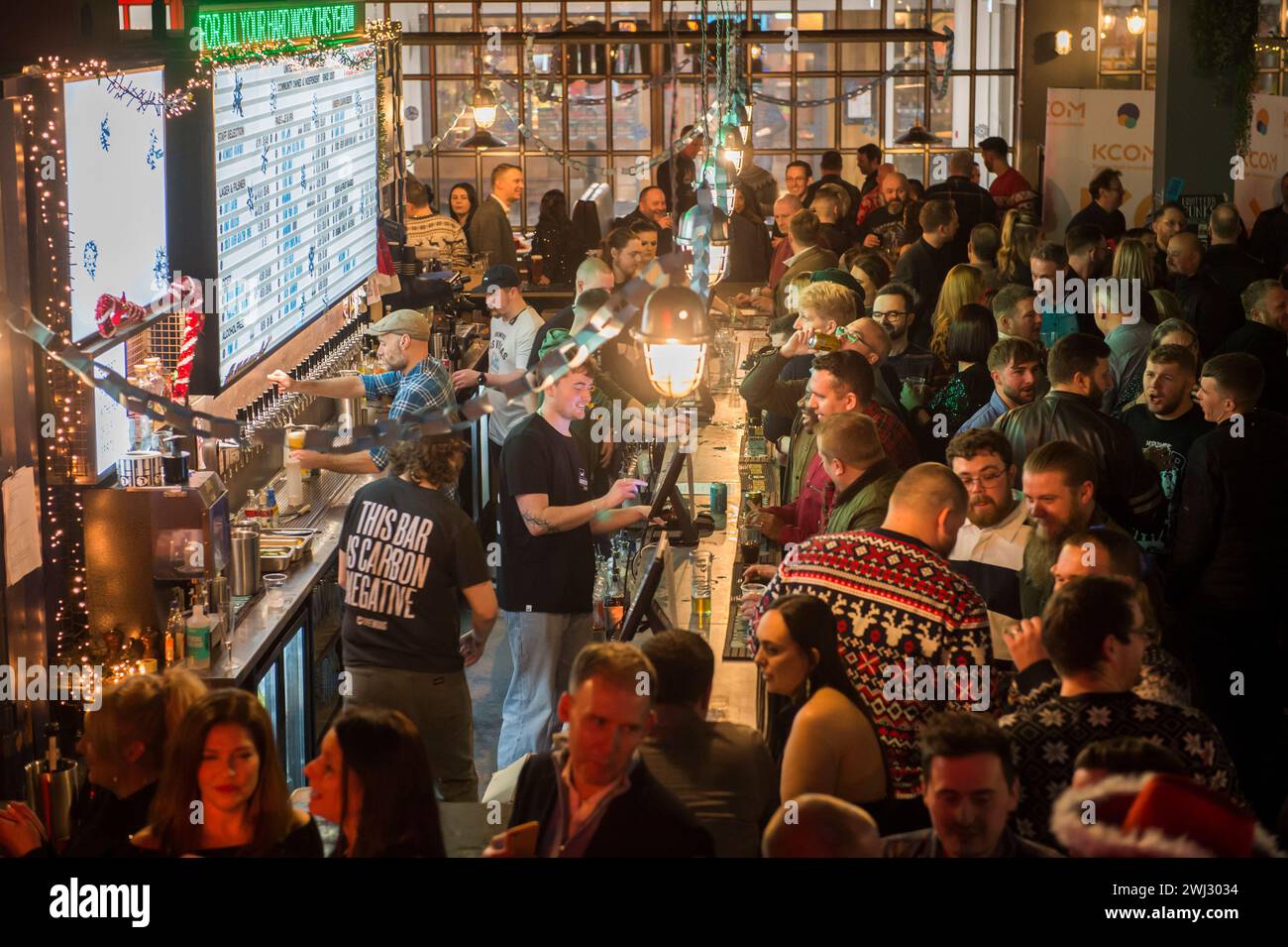 Eine voll bepackte Bar in Hull, East Yorkshire, nahe Weihnachten. Ein Barkeeper trägt ein T-Shirt „This Bar is Carbon negative“. Stockfoto