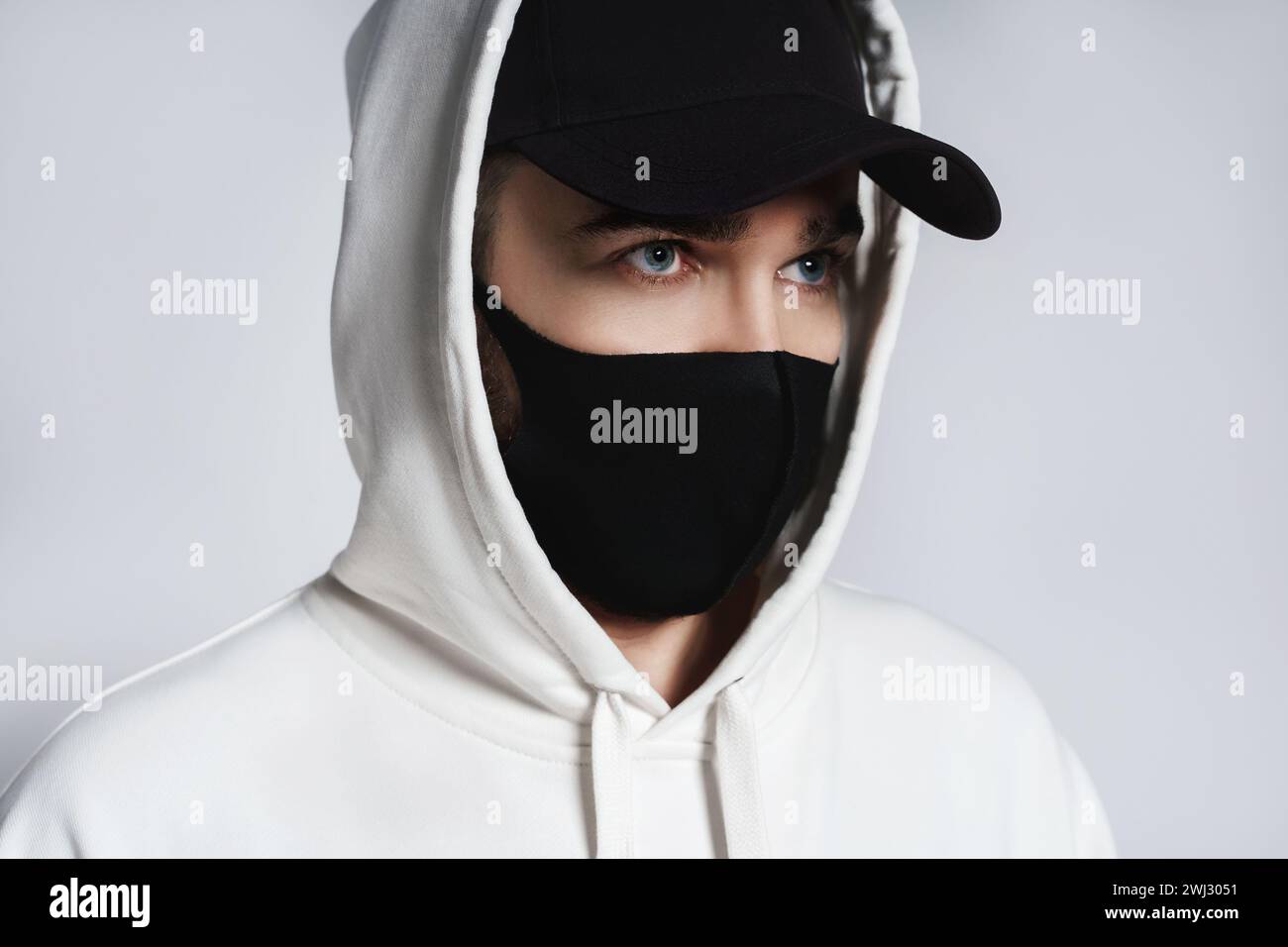 Mann mit weißem Hoodie, schwarzer Baseballmütze und Stoffmaske Stockfoto