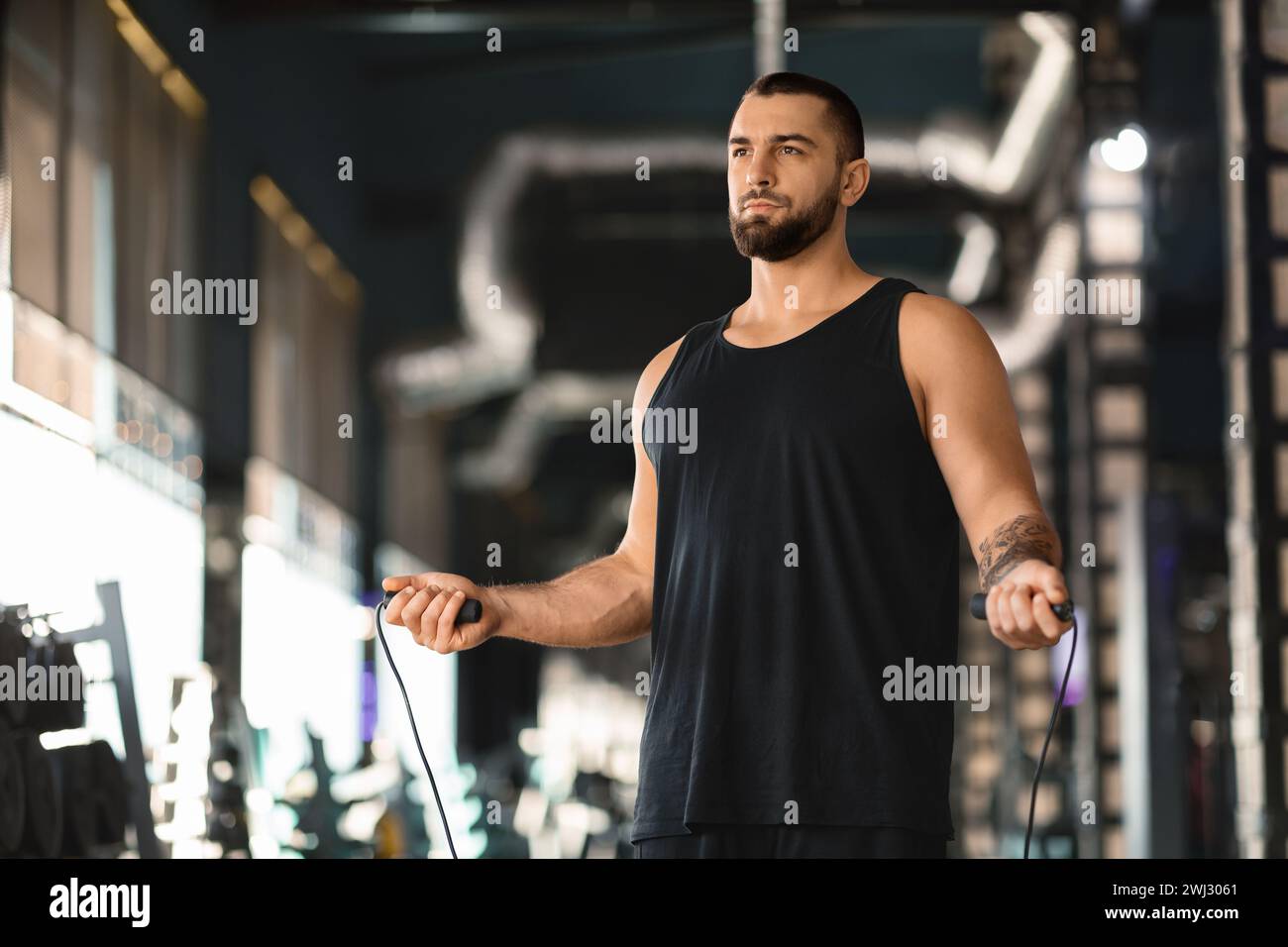Konzentrierter tätowierter männlicher Athlet mit Sprungseil in den Händen, der im Fitnessstudio steht Stockfoto