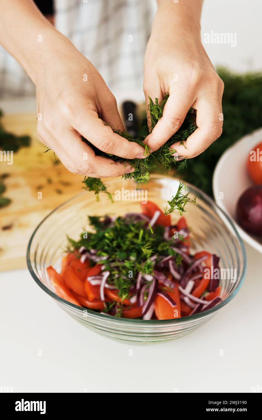 Weibliche Hände kochen vegetarischen Salat und fügen grünen Dill hinzu Stockfoto