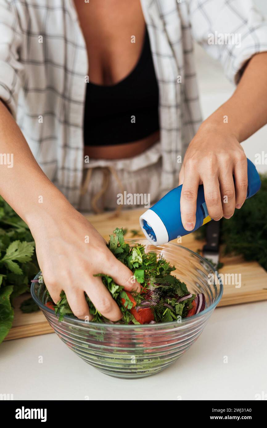 Weibliche Hände mischen vegetarischen Salat und geben das Salz dazu Stockfoto