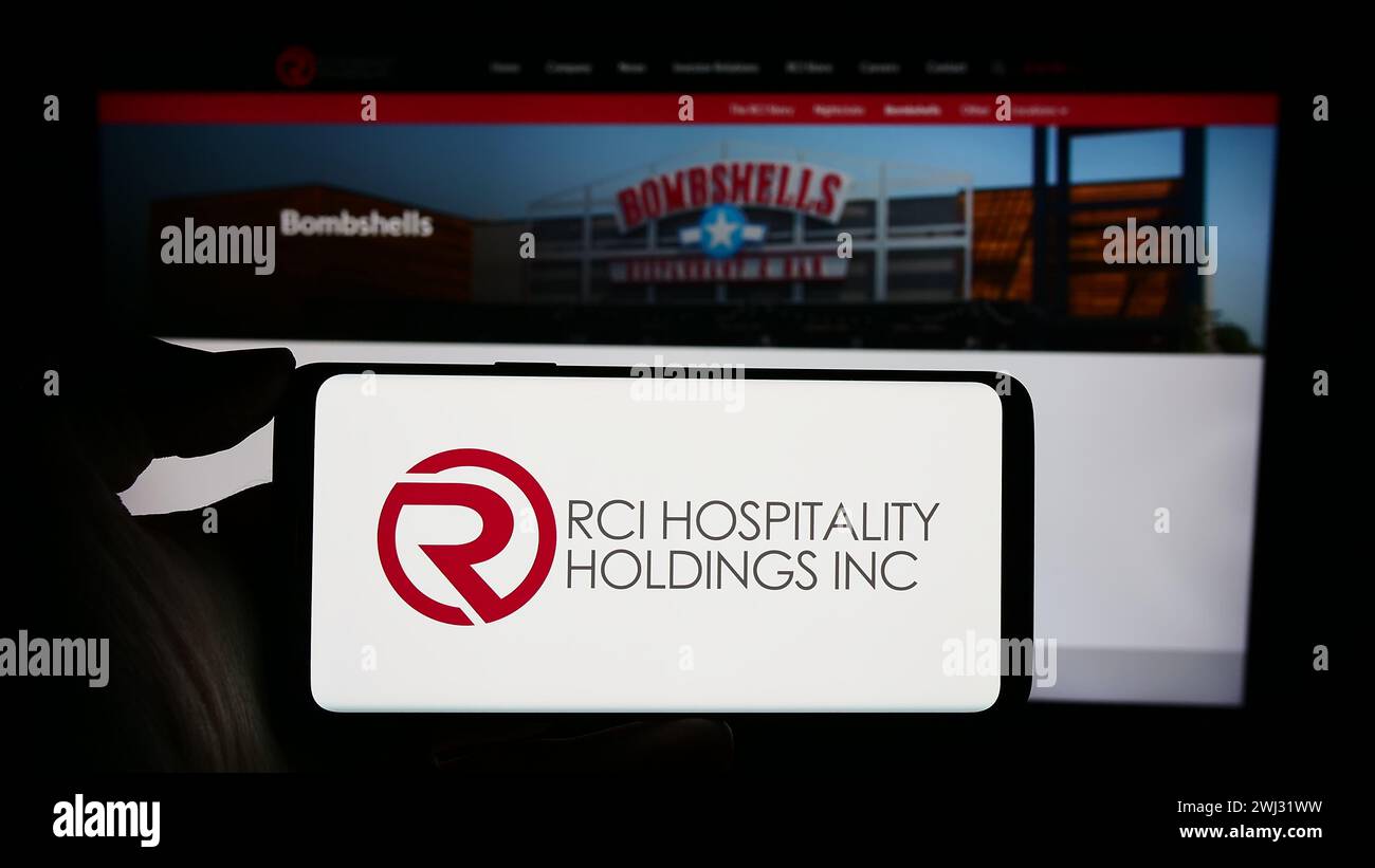Person, die ein Mobiltelefon mit dem Logo des US-Nachtclub-Unternehmens RCI Hospitality Holdings Inc. Vor der Webseite des Unternehmens hält. Schwerpunkt auf dem Display des Telefons. Stockfoto