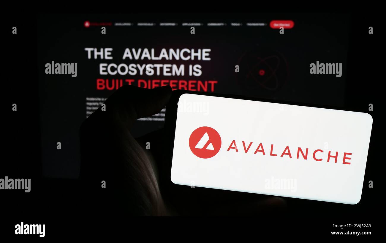 Person, die ein Mobiltelefon mit dem Logo des Blockchain-Unternehmens Avalanche (BVI) Inc. Hält (Avax Network) vor der Webseite. Schwerpunkt auf dem Display des Telefons. Stockfoto