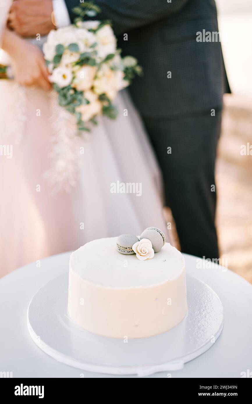 Der Bräutigam umarmt die Braut in der Nähe der Hochzeitstorte auf einem Stand auf dem Tisch. Abgeschnitten. Gesichtslos Stockfoto